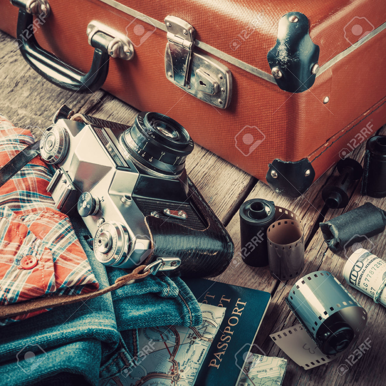 Old travel suitcase, sneakers, clothing, map, filmstrip and retro film camera on wooden background. Vintage stylized.